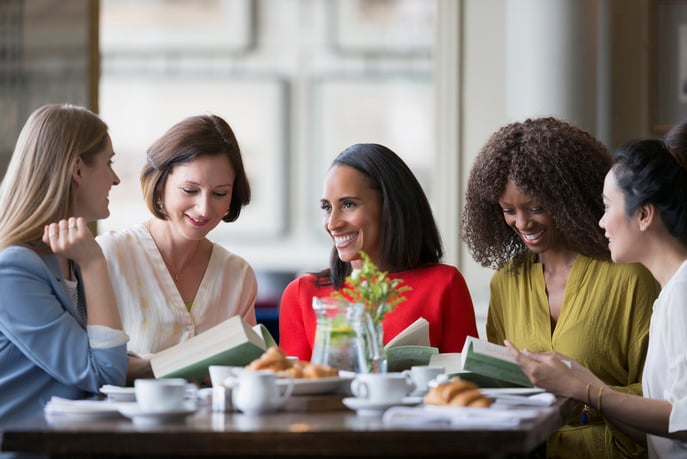 Women friends discussing book club book at restaurant table.